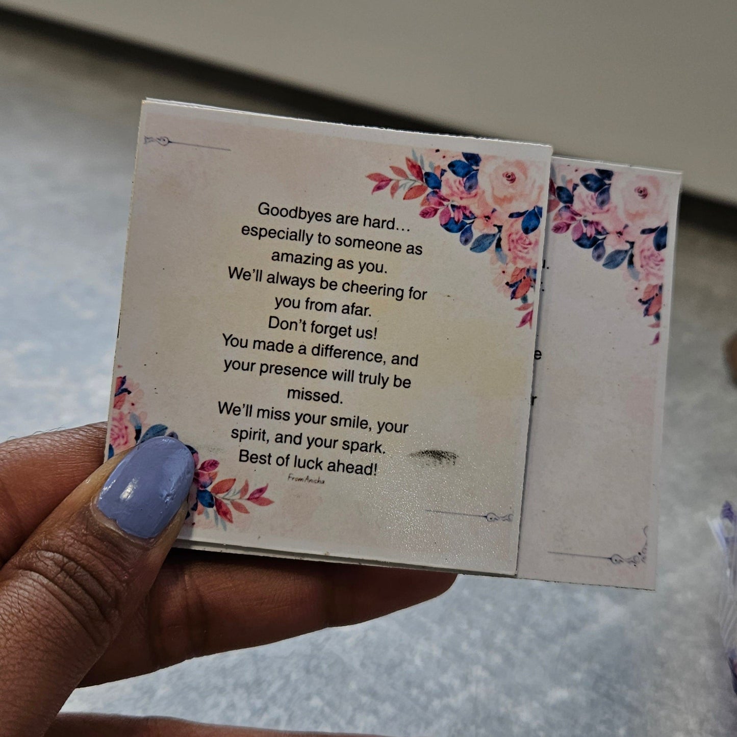 Hand holding a floral card with text on a textured surface